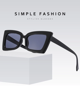 Close-up of oversized black square sunglasses displayed on a white geometric platform