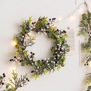 Christmas wreath with berries and LED lights on white wall for festive home decoration