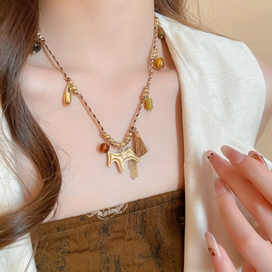 Close-up of woven rope necklace with tassel detail and golden horse charm pendant