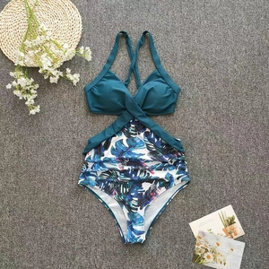 Flat lay of a one-piece monokini with teal halter top and tropical leaf print bottom