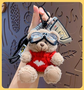 Detail of plush brown bear keychain wearing a red heart sweater and goggles on a lanyard
