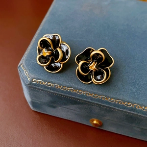 Close-up of vintage black camellia earrings with gold trim on a blue velvet jewelry box