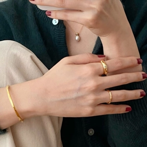 Detail of minimalist gold jewelry set featuring open bangle, rings, and pearl pendant