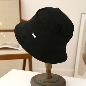 Detail of a black foldable bucket hat with a woven logo tag on a wooden stand