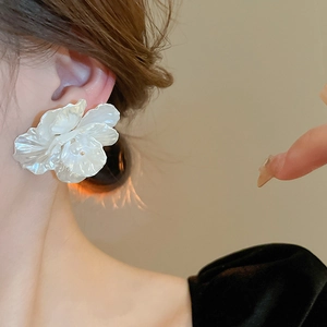 Detail of a large white acrylic floral earring with pearlescent finish and layered petals