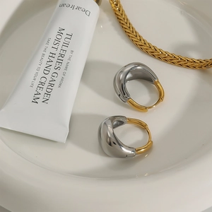 Two-tone geometric gold and silver stainless steel earrings on a ceramic dish