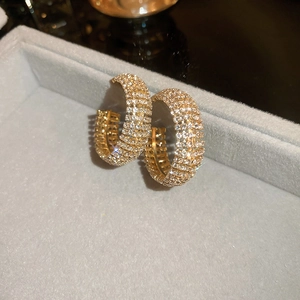 Macro di orecchini a cerchio a C in oro con pavé di cristalli su portagioie grigio
