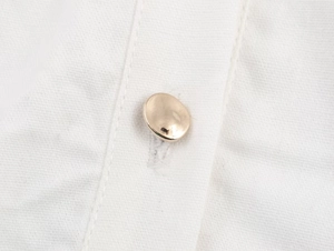 Gros plan de boutons dorés ovales sur un tissu de chemise en coton-lin blanc texturé
