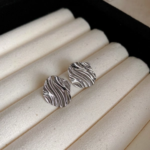 Macro shot of silver-colored twisted earrings with liquid-metal texture on beige velvet
