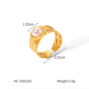 Detail of golden stainless steel open ring featuring a white pearl and brushed texture