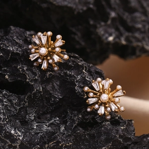 Macro shot of firework-shaped 18K gold earrings with pearls and crystals on dark rock