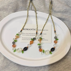 Colorful floral beaded necklaces with orange and green leaf charms on a white ceramic plate