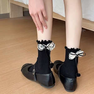 Detail of black crew socks with lace bows, pom-poms, and Mary Jane shoes
