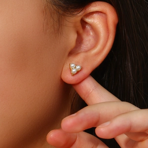 Close-up of model wearing gold triangular pearl earrings with three white pearls