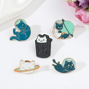 Close-up of assorted metal cat astronaut enamel pins on a white silk background