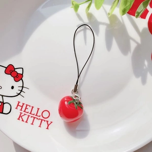 Detail shot of a realistic tomato pendant charm on a white ceramic plate with a black lanyard
