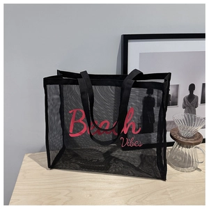Close-up of black mesh beach tote bag with Beach Vibes text on a light wood table