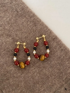 Detail of beaded hoop earrings with tiger eye stone and pearls on brown knit fabric