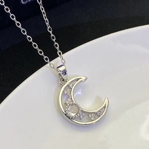 Macro shot of S925 silver moon pendant with sparkling white diamonds on a white surface