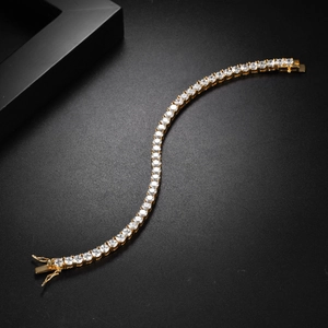 Detail of gold tennis bracelet with white zircons in S-curve pose on black background