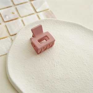 Close-up of a matte pink square hair claw clip on a white ceramic textured tray