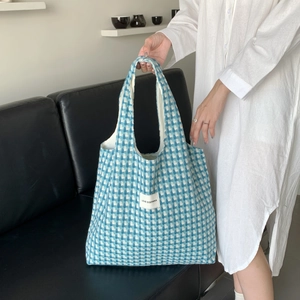 Close-up of blue and white checkered knit tote bag with brand label held by a model