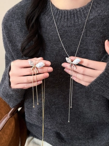 Close-up of butterfly pearl necklaces with rhinestone tassels on grey sweater