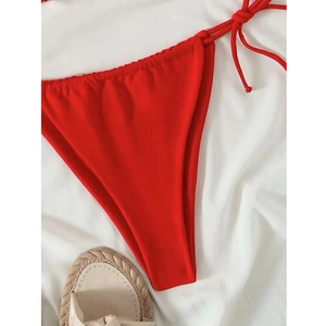 Detail of red string bikini bottoms with side ties on a white fabric background