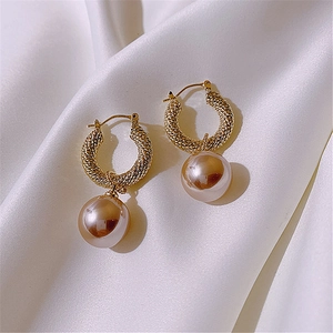 Macro shot of gold twist hoop earrings with large pearls on white silk fabric background