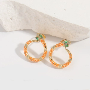Detail of snake hoop earrings with orange enamel, gold trim and green gemstone eyes