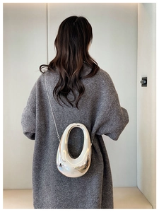 Model showing a silver sculptural oval crossbody bag with a reflective metallic finish