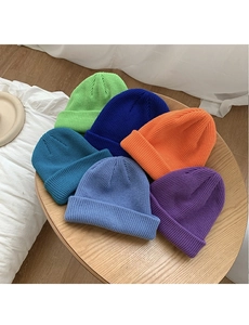 Flat lay of colorful ribbed knit beanies in green, blue, and orange on wooden table