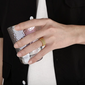Detail of a gold mesh woven stainless steel ring worn on a finger holding a textured glass