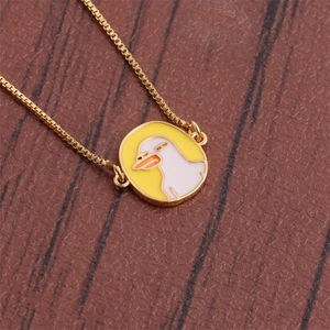 Detail of a gold-plated necklace featuring a round white duck pendant on a yellow base