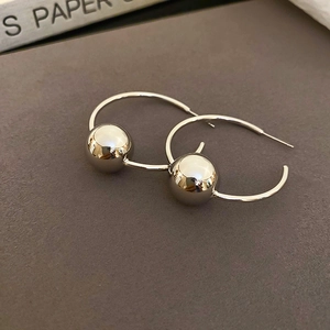 Dettaglio di orecchini a cerchio geometrici argento con sfera di metallo lucido su grigio