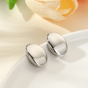 Close-up of minimalist silver oval stud earrings on a ceramic tray with floral background