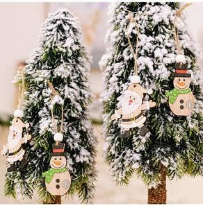 Detail of wooden Santa and Snowman ornaments hanging on a snow-covered pine branch