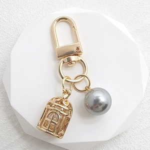 Detailed close-up of golden birdcage pendant with a grey pearl on a polished keychain