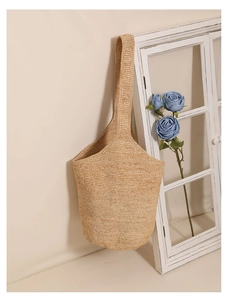 Detail view of a large raffia bucket bag hanging against a white wall in beach style
