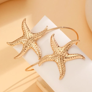 Detailed close-up of two golden starfish cuff bracelets with textured finish on a white surface