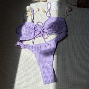 Detailaufnahme des lila strukturierten Bikinis mit Muscheln auf Strandmatte