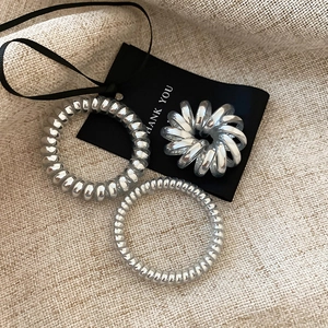 Close-up of three metallic silver spiral hair ties on minimalist cream textured fabric