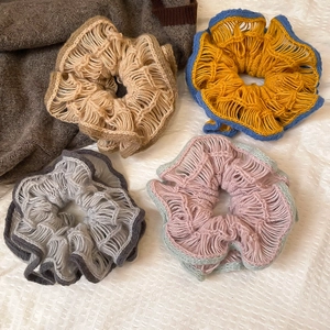 Detail of four colorful knit hollow crochet hair scrunchies on white textured fabric
