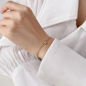 Close-up of a gold chain bracelet with a rectangular clear crystal on a model wrist