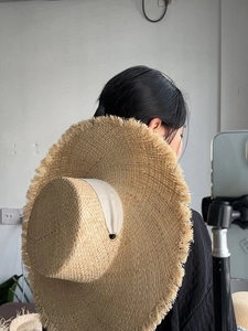 Detail of raffia sun hat featuring frayed edges and wide ribbon trim from a back view