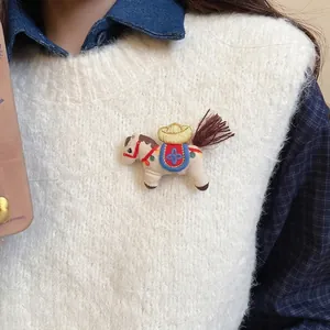 Cute knitted horse brooch with golden ingot and embroidery on beige velvet fabric