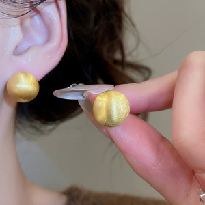 Macro detail of golden brushed metal spherical stud earrings on model for daily wear