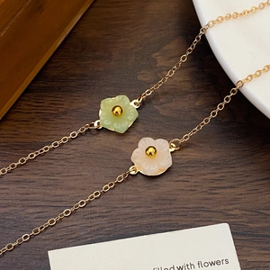 Elegant gold flower bracelet with white shell and green floral pendants on a wooden table