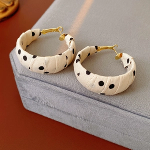 Dettaglio macro di orecchini a cerchio in tessuto beige a pois con chiusure dorate