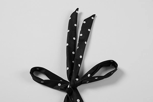 Detail of a black silk halter dress featuring white polka dots and a tied bow neckline